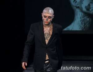 Фото мужчины с татуировкой черепа на лице, одетого в смокинг. Татуировка выполнена в черно-серых тонах с высокой детализацией.